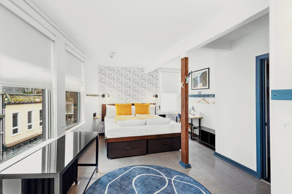 A modern bedroom with a large bed, a desk, and a view of the city.