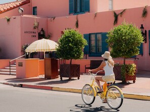 Una dona anava en bicicleta groga amb un cisteller davant d'un edifici rosa amb la placa "Arizona Inn".