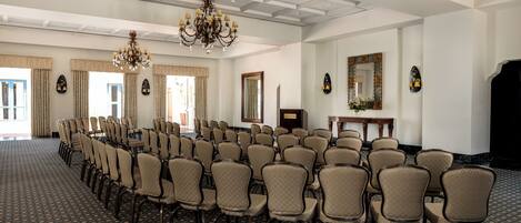 A conference room with rows of chairs, a chandelier, and a large mirror on the wall.