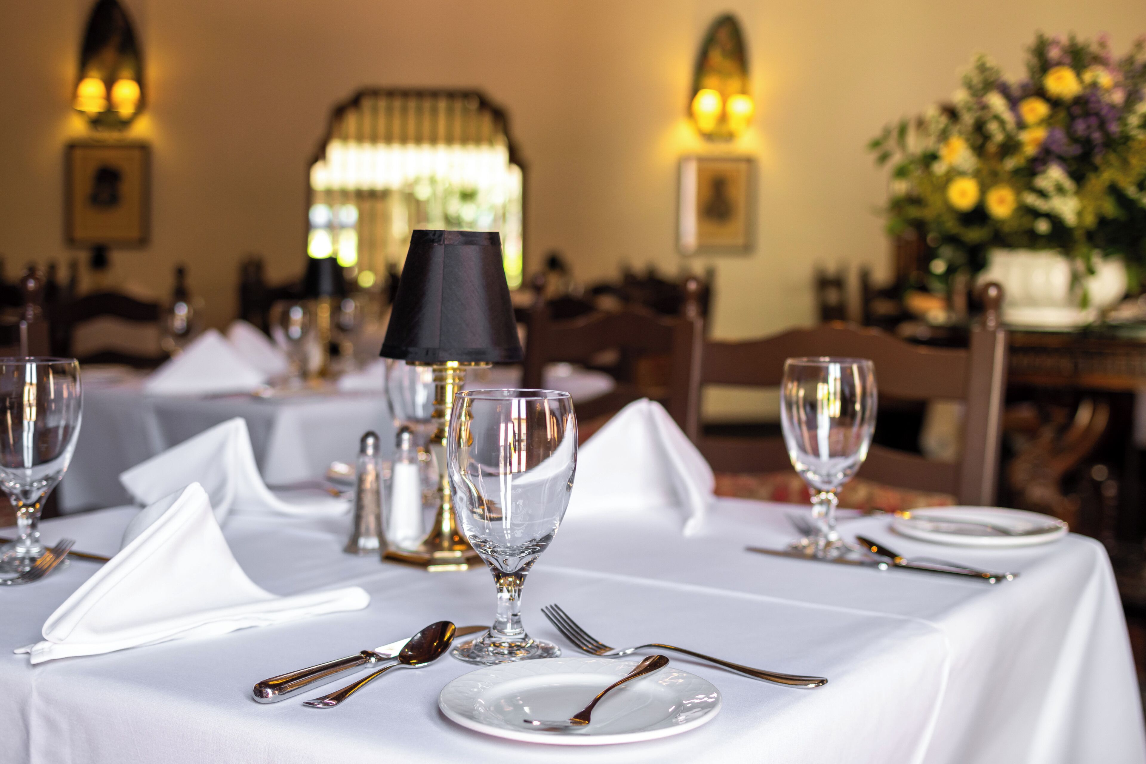 Une table à manger dressée avec une nappe blanche, des assiettes, des couverts et un verre.