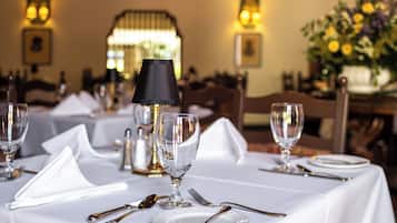 Une table à manger dressée avec une nappe blanche, des assiettes, des couverts et un verre.
