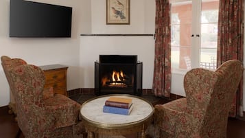 A living room with a fireplace, two armchairs, a coffee table with books, a television, and a framed picture on the wall.