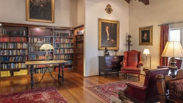 A library with bookshelves, a reading table, a red armchair, and a fireplace.