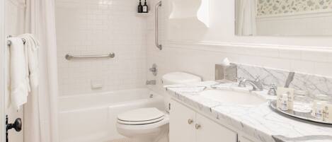 A bathroom with a bathtub, toilet, and vanity with a marble countertop.
