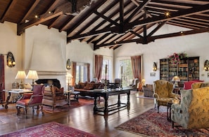 A spacious living room with wooden beams, a fireplace, and a large bookcase.