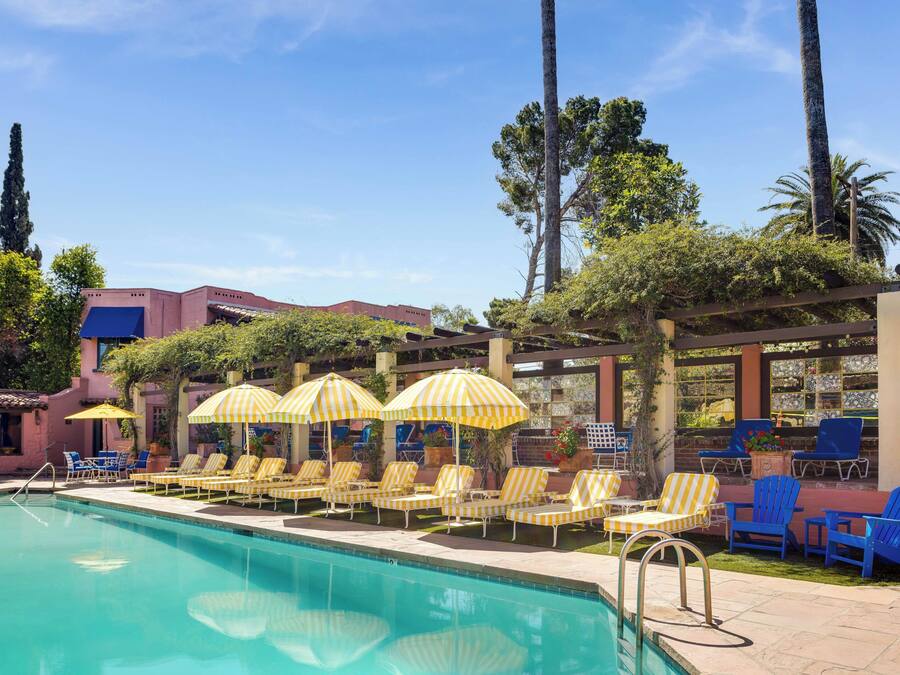A pool area with lounge chairs and umbrellas, surrounded by trees and a building.