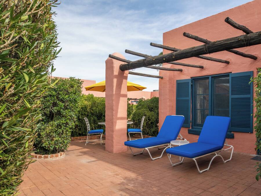 Un patio con sillones azules, una pérgola de madera y un paraguas amarillo.