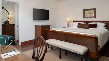 A hotel room with a bed, bedside table, chair, desk, TV, and a framed picture on the wall.