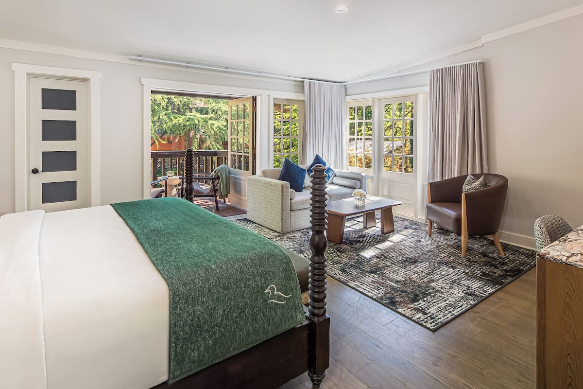 Una habitación de hotel con cama, sofá, sillón, una mesita y vistas al exterior.