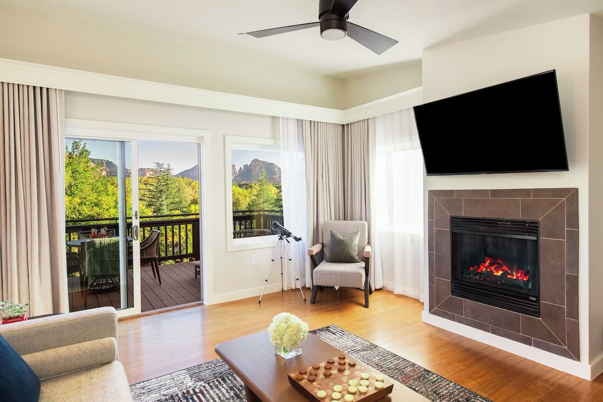 Una sala de estar con chimenea, televisor, una silla y vistas a un balcón con mesa y sillas.