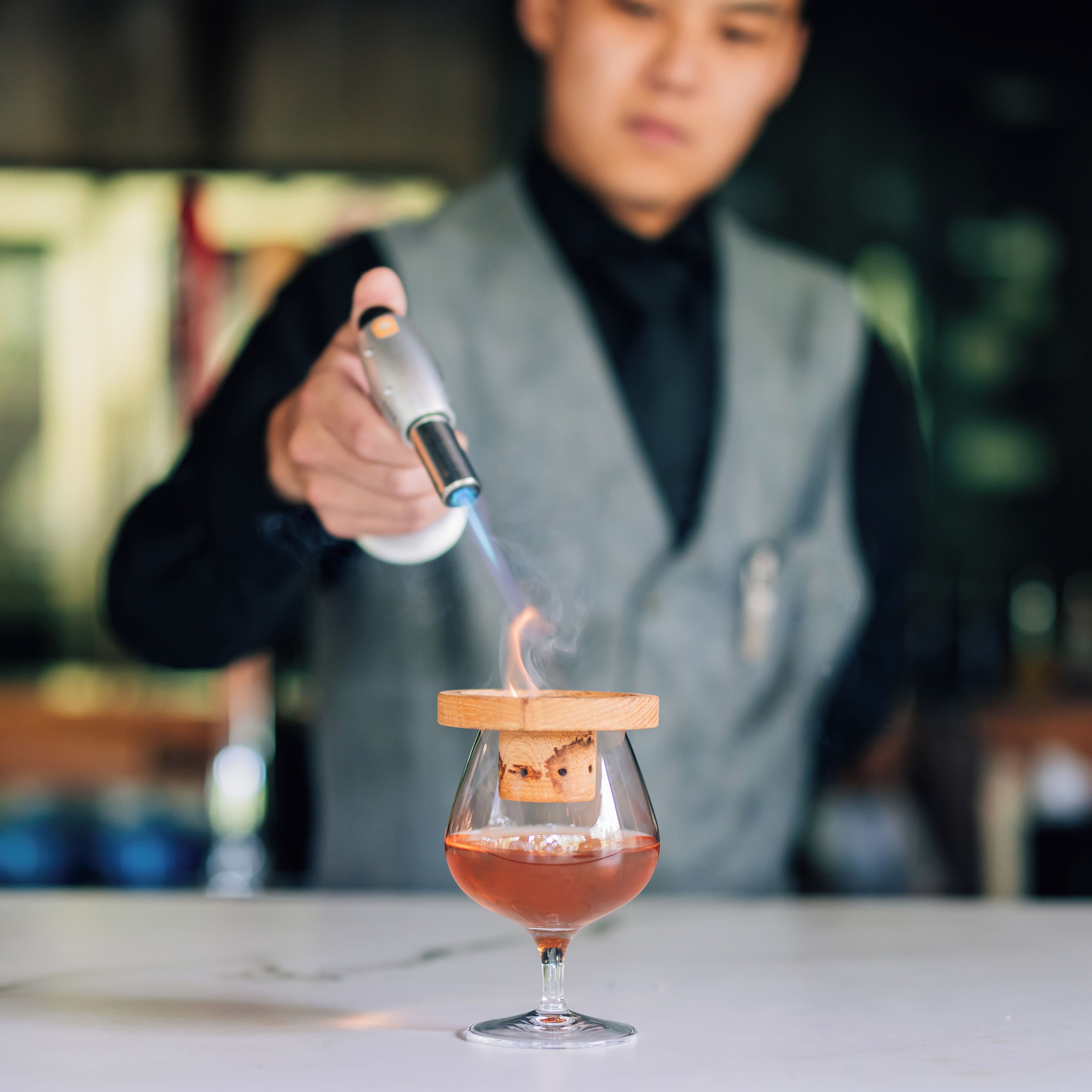 Un barman prépare un cocktail en y ajoutant une garniture flambée.