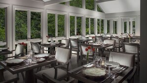 Ein Restaurant mit mehreren Tischen, großen Fenstern mit Blick auf Grünflächen und einer hohen Decke.