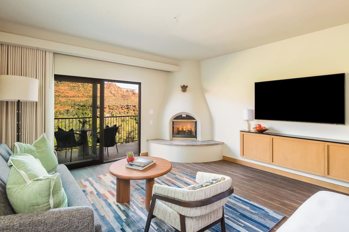 Habitación de hotel con sofá, sillón, televisión, chimenea y un balcón con mobiliario exterior.