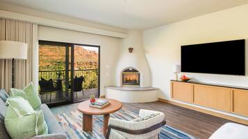 Ein Hotelzimmer mit einer Couch, einem Sessel, einem Fernseher, einem Kamin und einem Balkon mit Gartenmöbeln.
