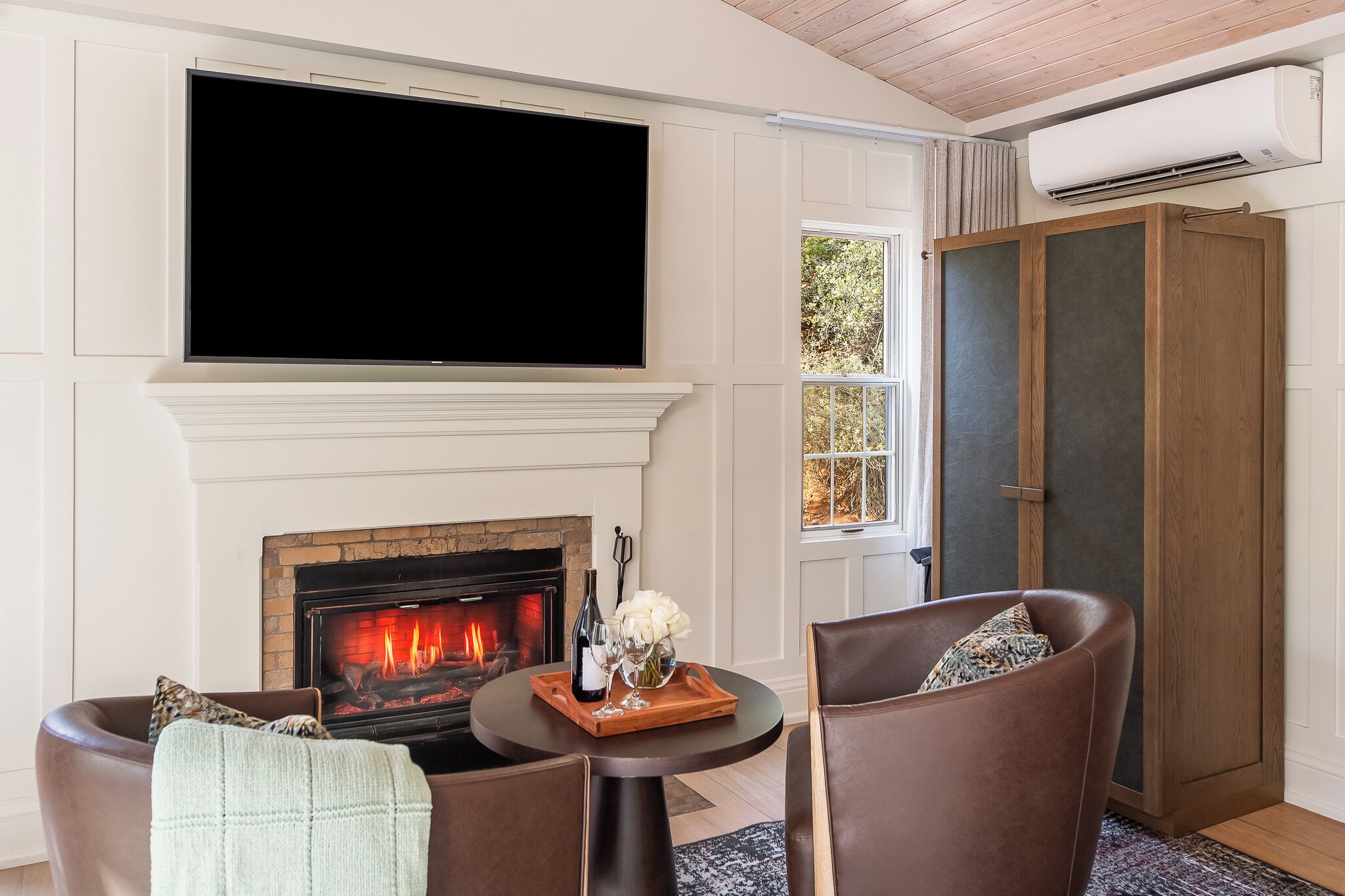 A living room with a fireplace, a flat-screen TV, and a large wooden cabinet.