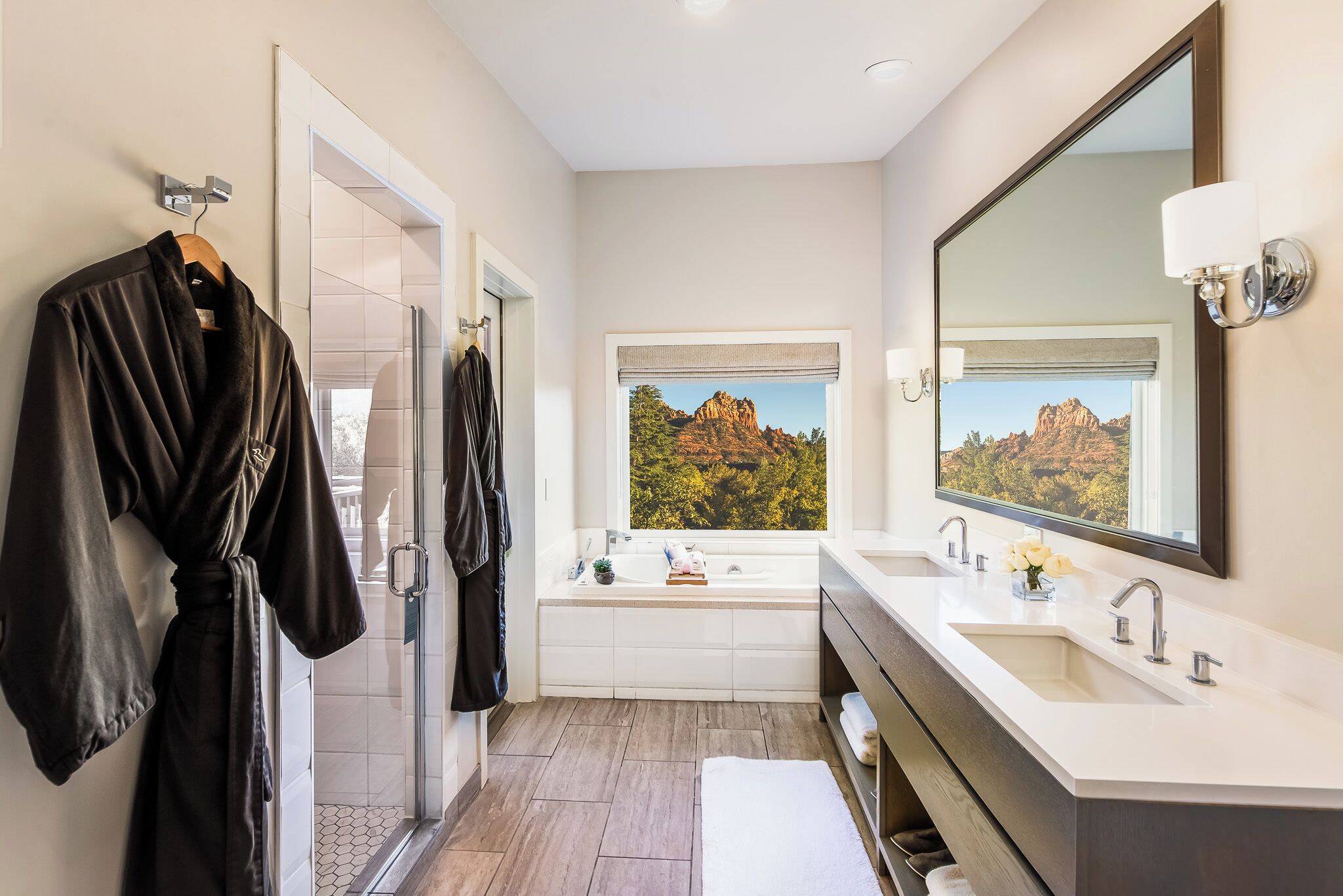 A modern bathroom with a large window, a bathtub, and a vanity with a mirror.
