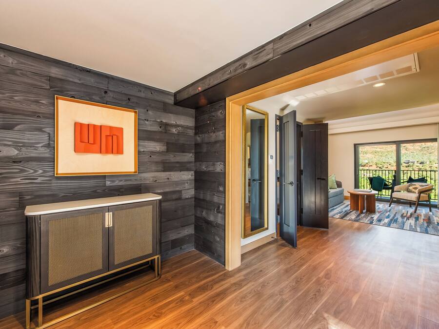 A modern interior with a dark wood panel wall, a radiator, and a view to a balcony with outdoor furniture.