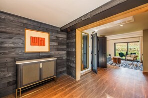 A modern interior with a dark wood panel wall, a radiator, and a view to a balcony with outdoor furniture.