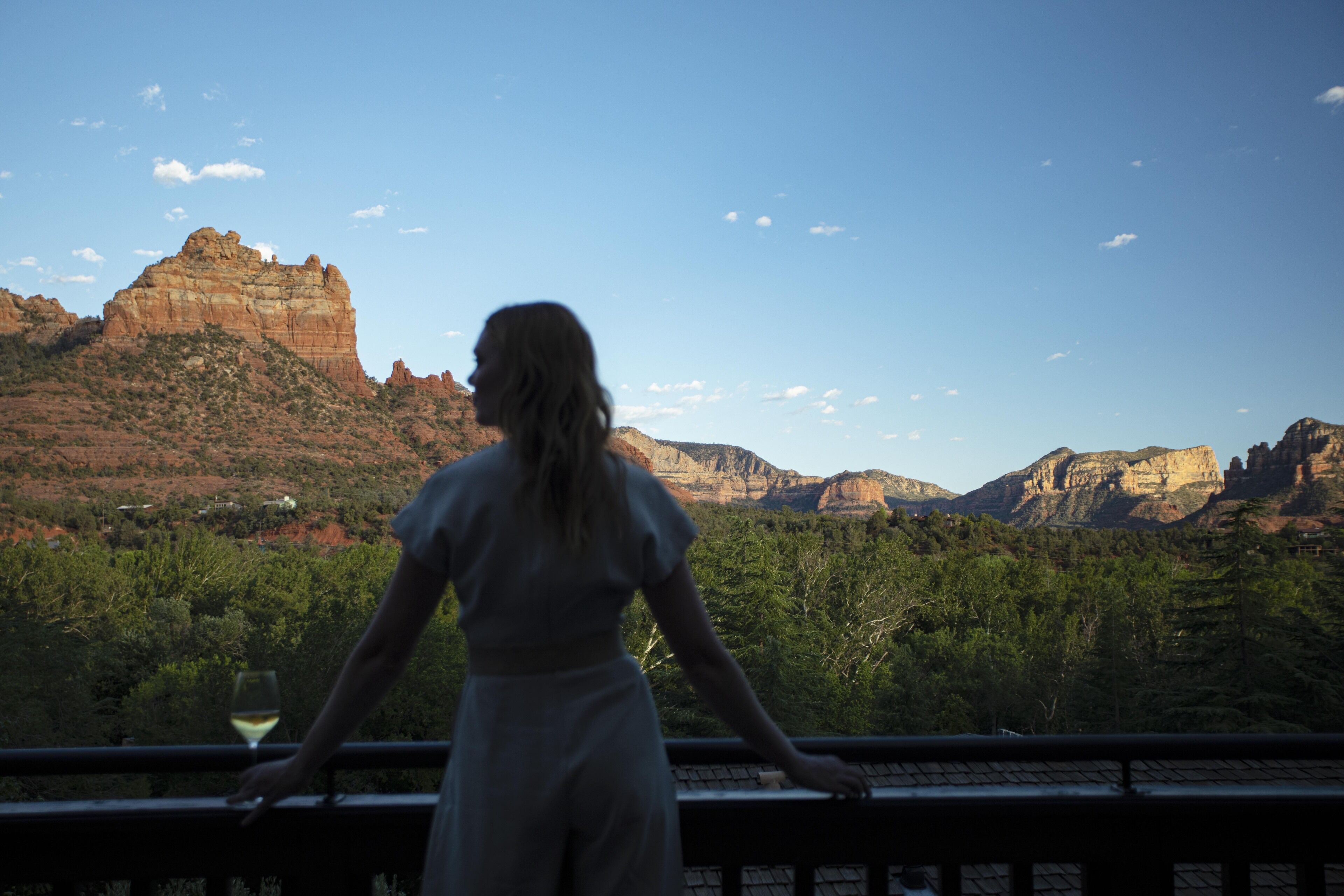 A person standing by a railing with a view of red rock formations and green trees.
