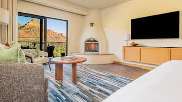 A hotel room with a large window, a fireplace, a television, and a bed.