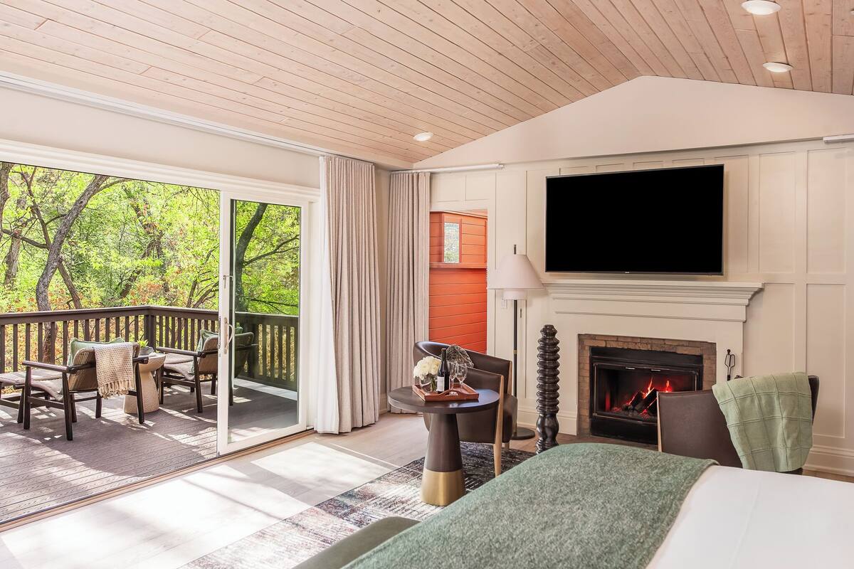 Una habitación con chimenea, televisión, balcón con sillas y cama.