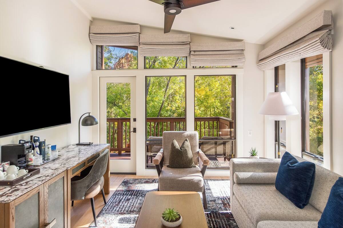 Una sala de estar moderna con una televisión de pantalla plana, un sofá, una silla, una mesa de centro y un comedor con mesa y sillas.