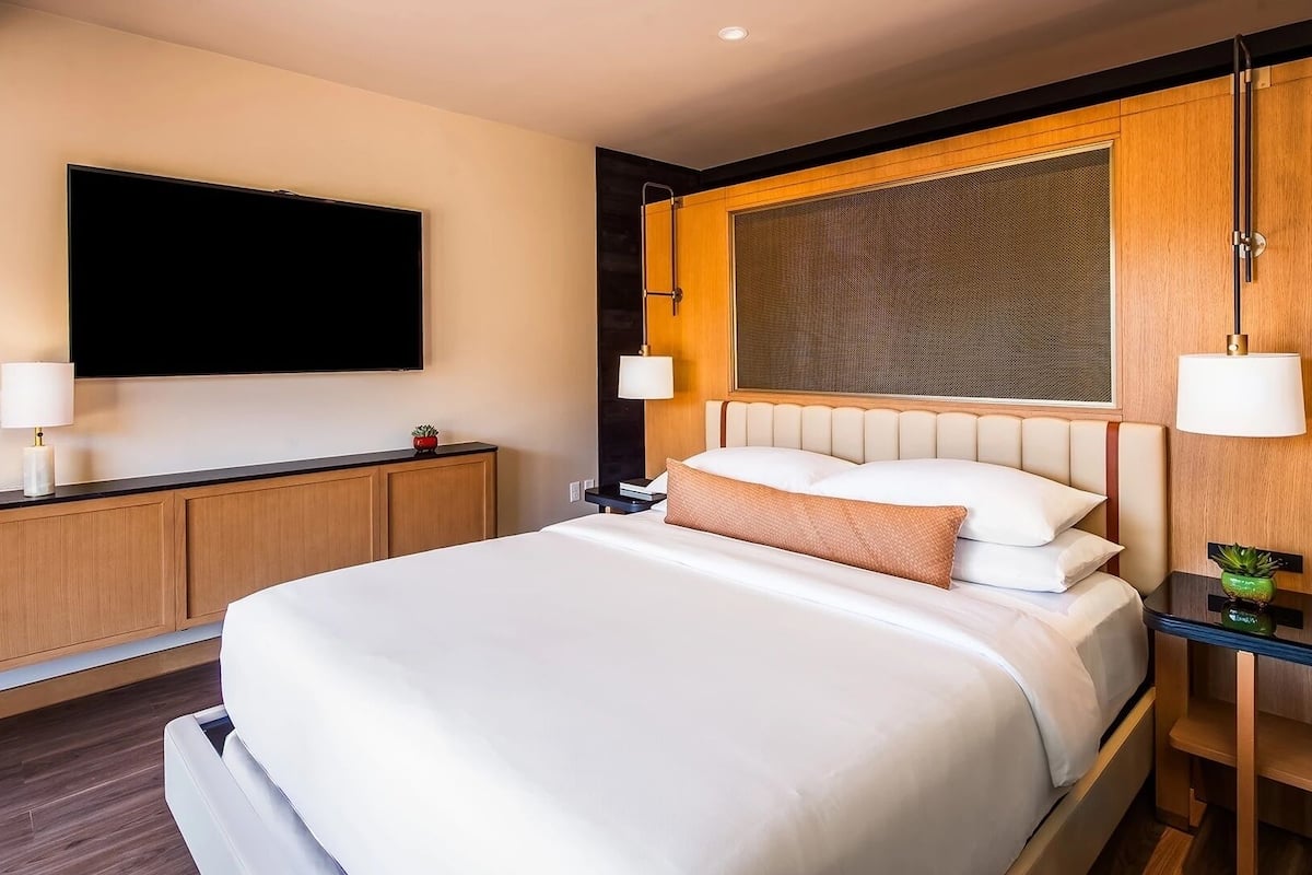 Habitación de hotel con una cama grande, un televisor de pantalla plana en la pared, cabecero de madera y lámparas de noche.