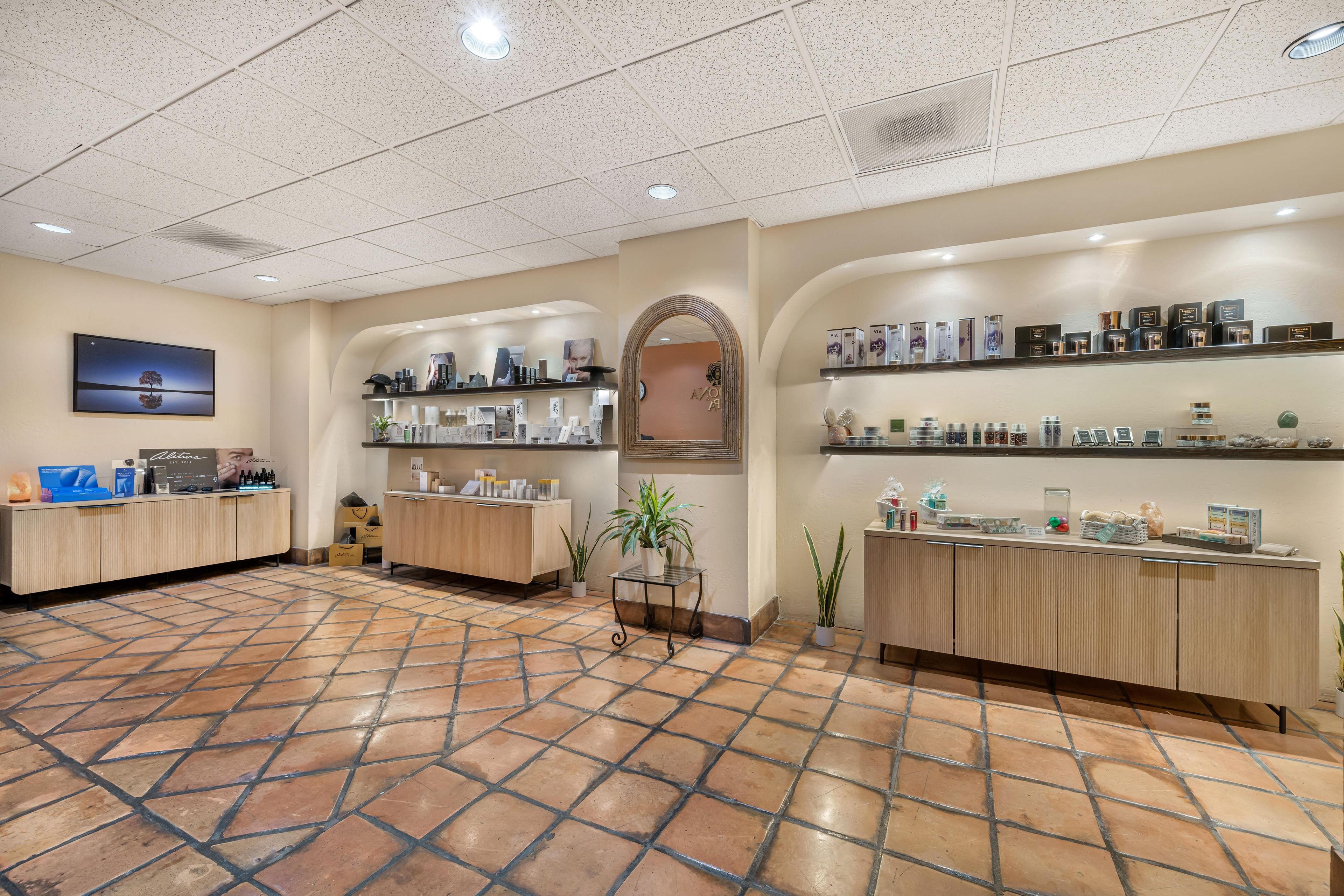 A spacious lobby with a tiled floor, wooden reception desks, and shelves stocked with products.