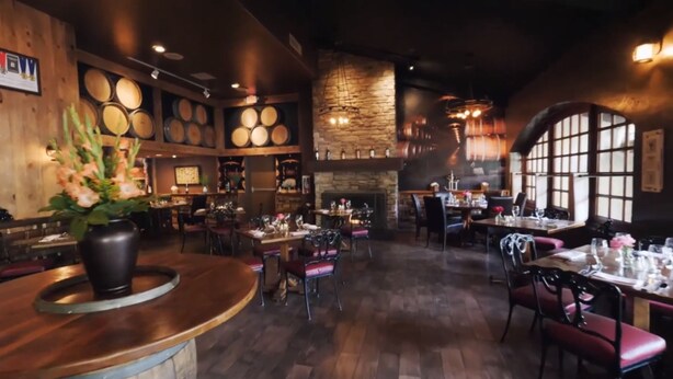 A restaurant interior with wooden tables, red chairs, a stone fireplace, and a wall decorated with circular objects.