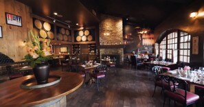 Interior de restaurante con mesas de madera, sillas rojas, chimenea de piedra y pared decorada con objetos circulares.