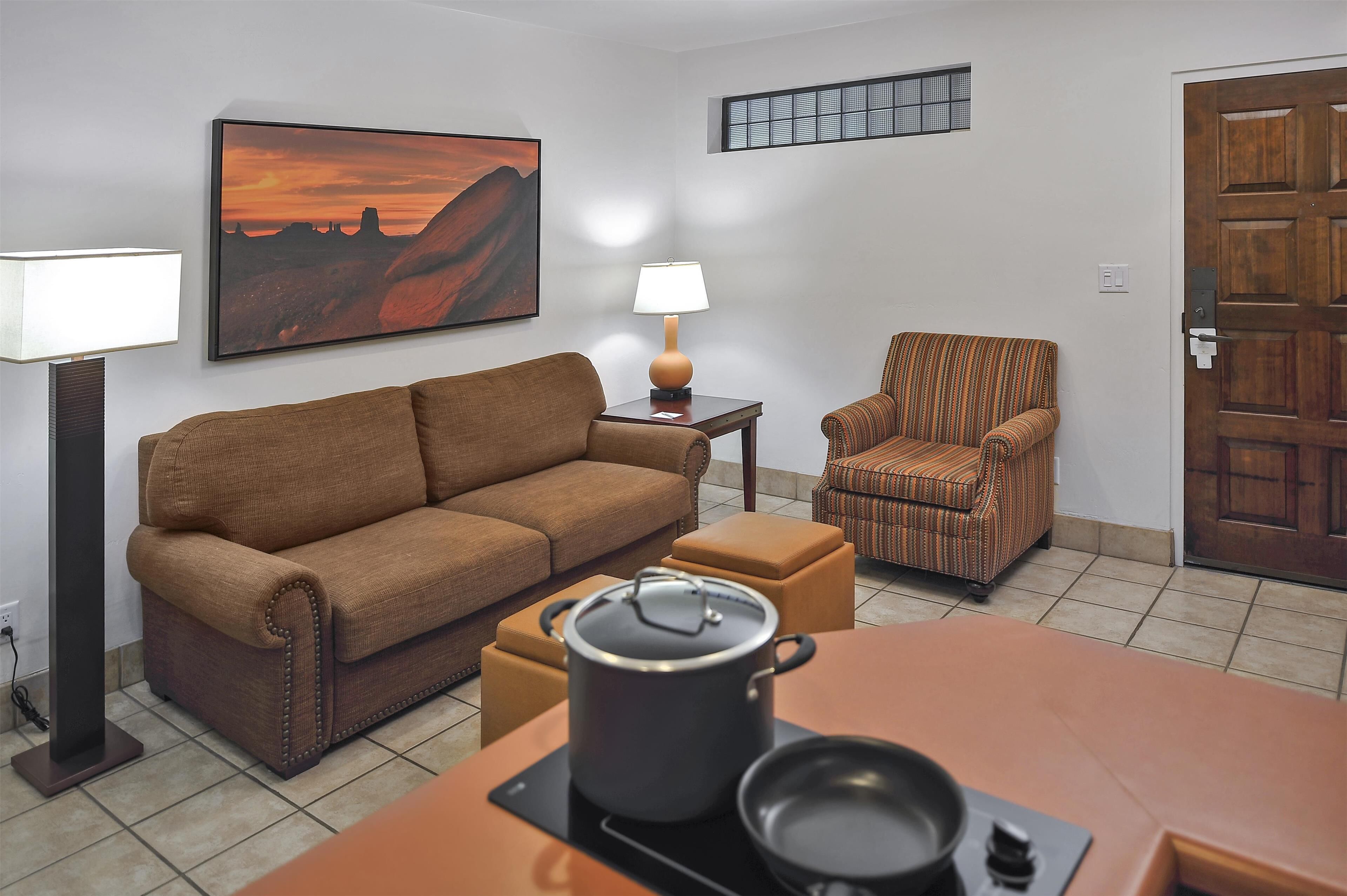 Una sala de estar con sofá, sillón, mesa con una olla, lámpara y un cuadro en la pared.