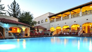 A swimming pool with lounge chairs and a building with arched windows and balconies.