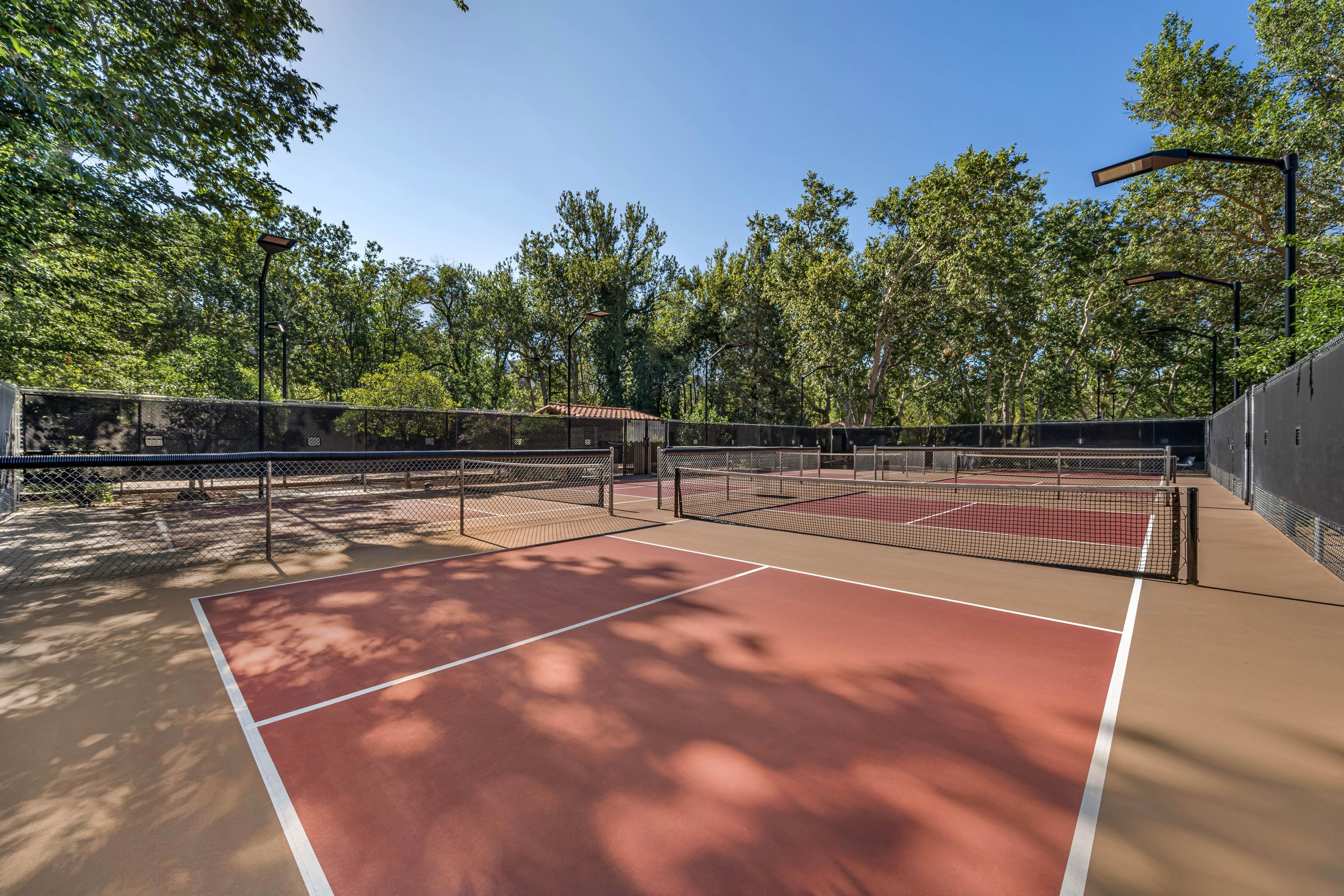 A tennis court with a net, surrounded by trees and a fence.