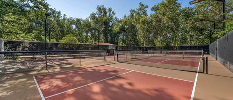 A tennis court with a net, surrounded by trees and a fence.