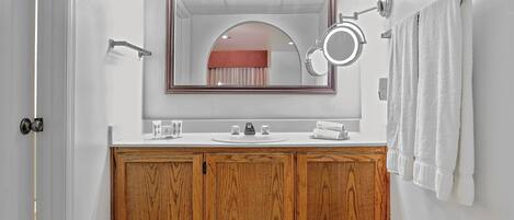 Un baño con tocador de madera, un espejo, un perchero para toallas y un lavamanos.