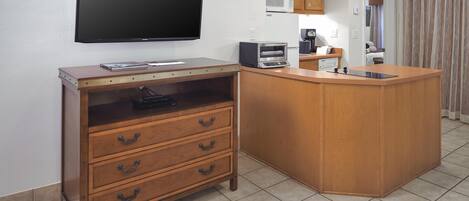 A compact kitchen with a flat-screen TV, wooden cabinetry, a microwave, and a coffee maker.