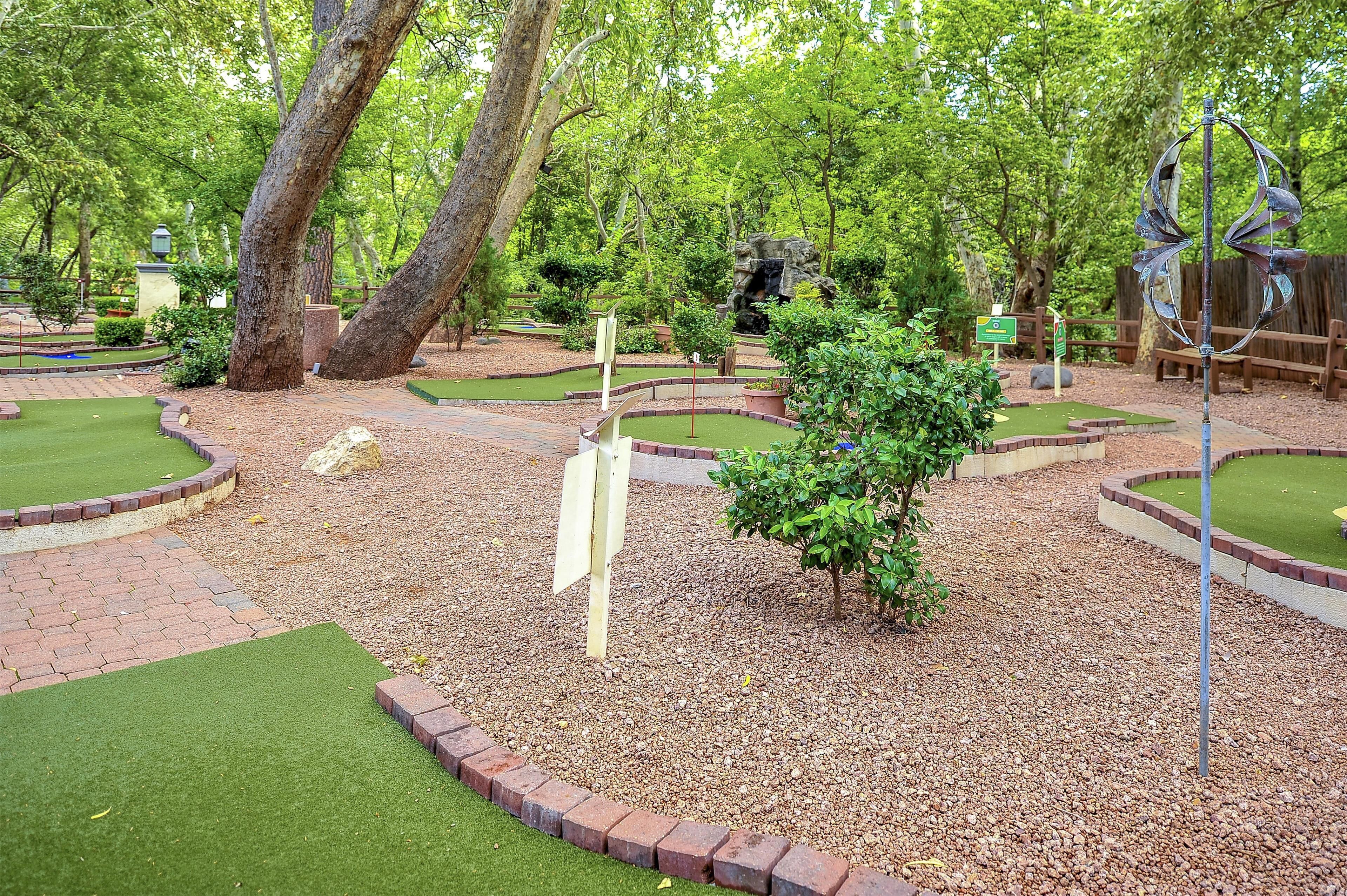 Un parcours de mini-golf avec un green d’entraînement, un petit arbre et un panneau indicateur.