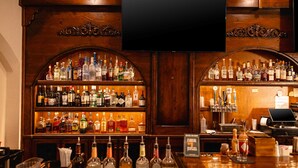 A bar area with shelves of liquor bottles, a flat-screen TV, and a cash register.