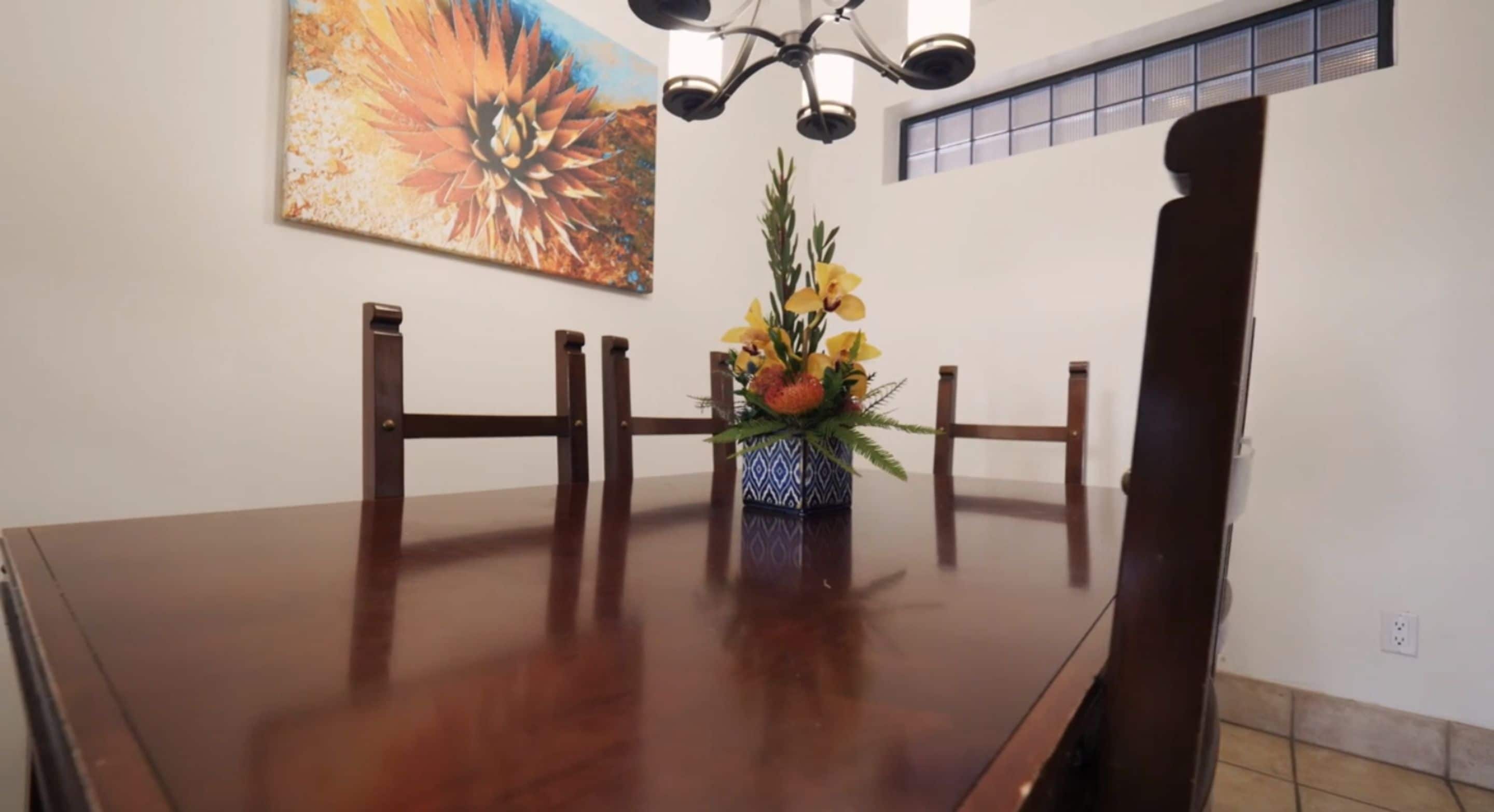 A dining table with chairs, a vase with flowers, and a painting on the wall.
