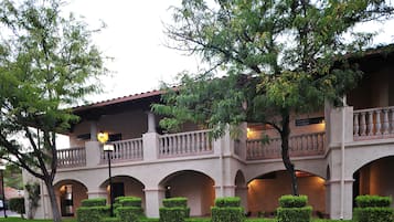 Classic hotel with arches and a balcony, surrounded by lush greenery.