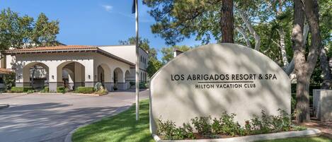 A sign for Los Abrigados Resort & Spa, Hilton Vacation Club, with a clear view of the building's architecture and a well-maintained lawn.
