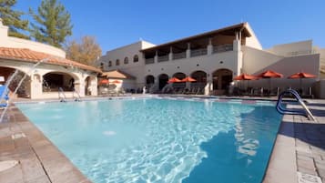 A swimming pool with lounge chairs and umbrellas, surrounded by a building with arches and a balcony.