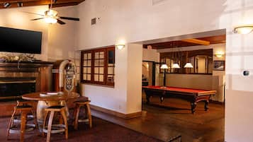 Uma sala de bilhar com mesa de sinuca, banquetas de madeira e um jukebox.