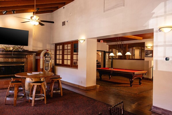 Una sala de billar con mesa de pool, taburetes de madera y un jukebox.