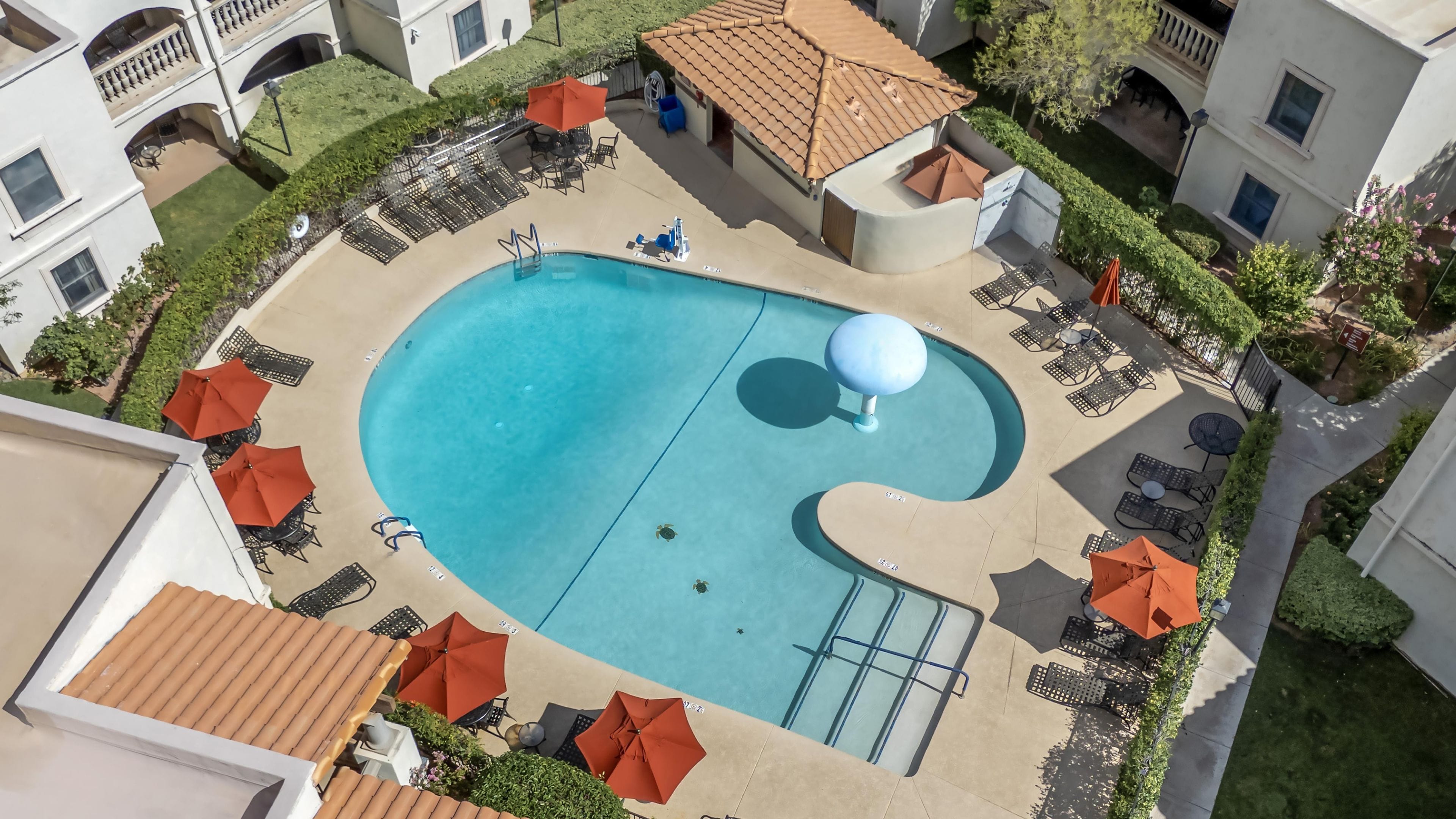 Ein Luftbild eines Hotels mit Schwimmbad, Liegestühlen und Sonnenschirmen.