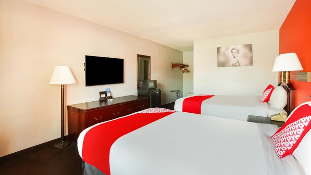 A hotel room with two beds, a flat-screen TV, a desk with a lamp, a dresser, and a microwave.
