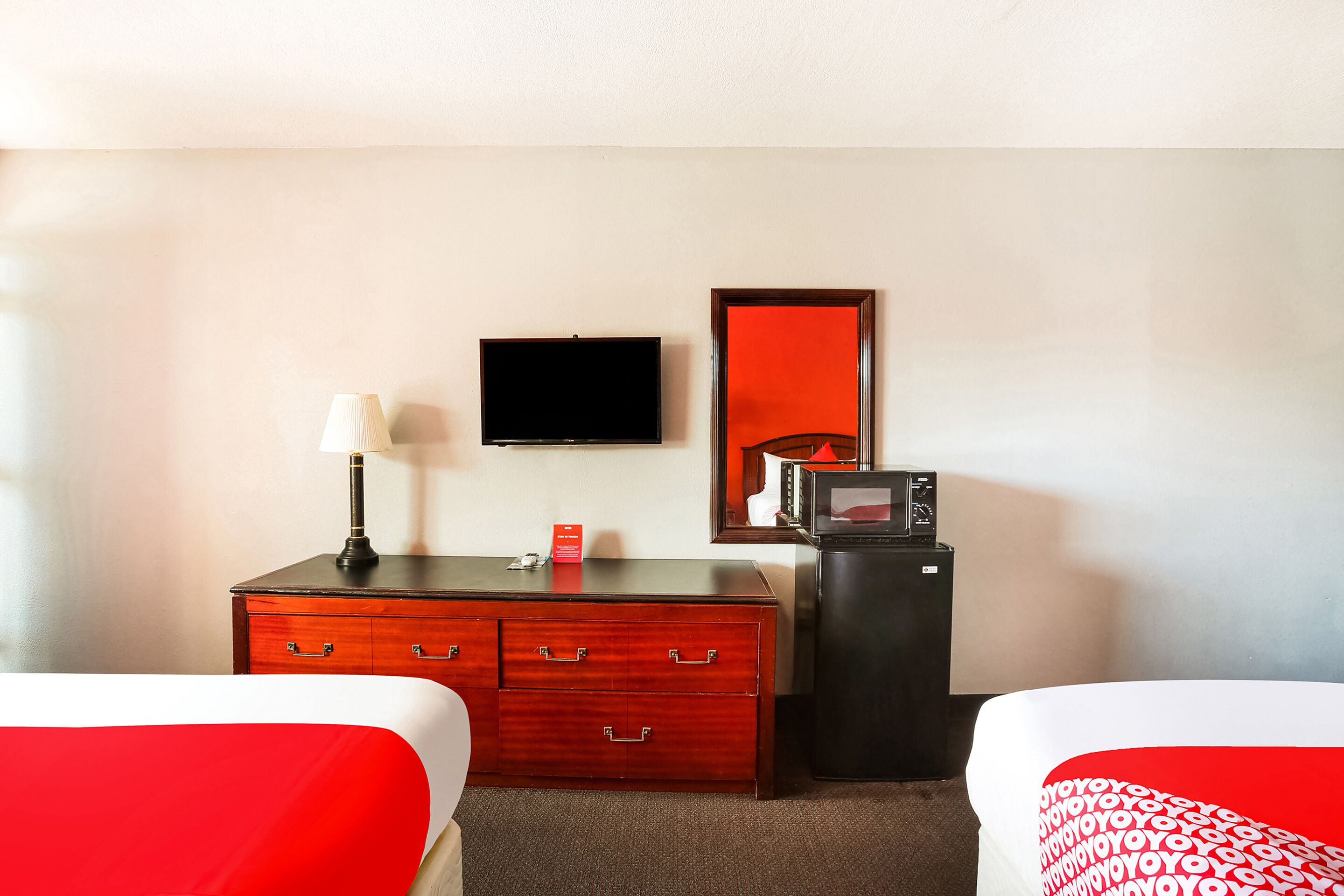 Una camera d'albergo con due letti, una televisione, un minibar e uno specchio.