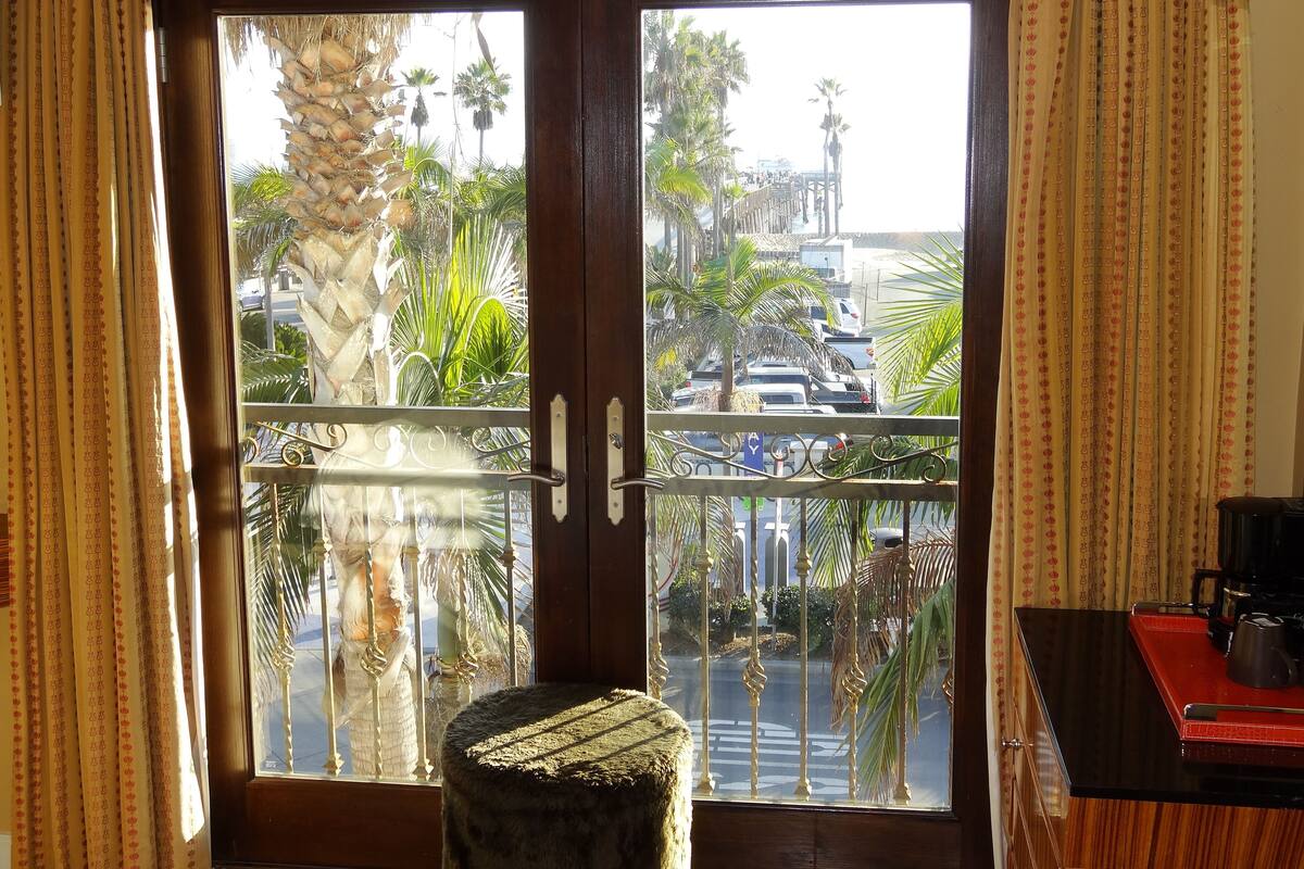 A room with a large window overlooking a street with palm trees and parked cars.
