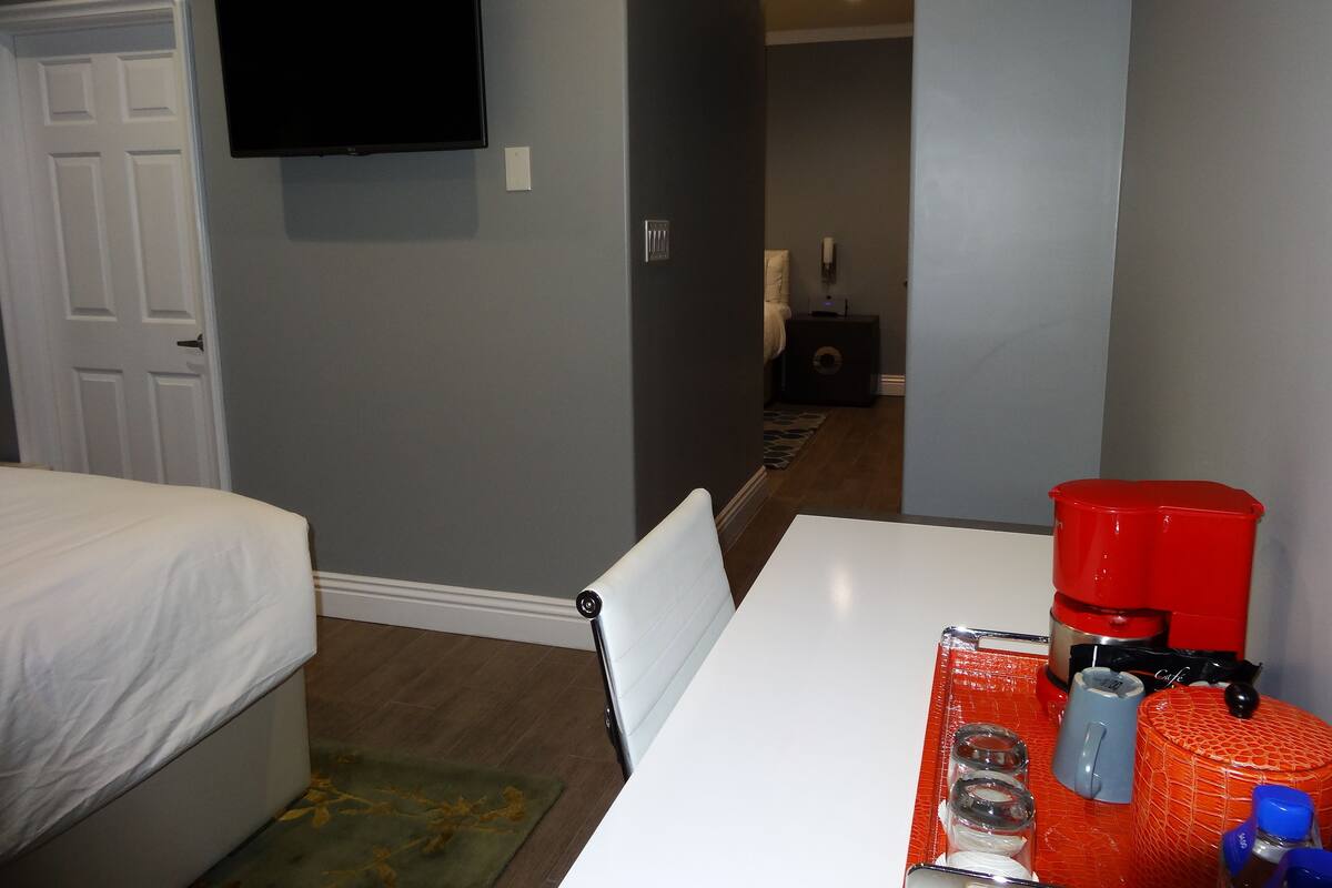 A hotel room with a bed, a desk with a coffee maker, and a TV on the wall.
