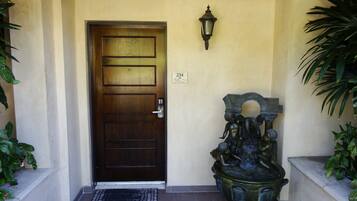 A wooden door with a metal handle and a doormat. There is a wall-mounted light fixture above the door and a decorative sculpture to the right.